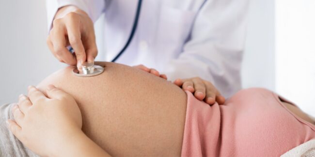 n obstetrician using a stethoscope on a pregnant woman's tummy.